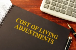 Journal On Desk Below Calculator With Title Cost Of Living Adjustment Printed On Top