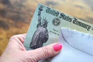 Older Woman's Hand With Pink Nail Polish On Thumb Holding Social Security Disability Benefits Check