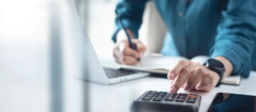 Person using a calculator and taking notes at a laptop while reviewing 2026 SSDI benefit amounts